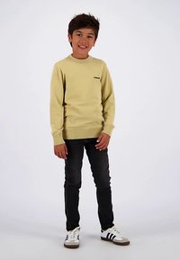 Light yellow sweater with round neckline and ribbed cuffs, paired with dark skinny jeans and white shoes with black stripes.
