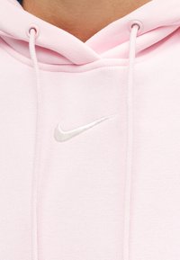 Κοντινό πλάνο ροζ φόρμας με λευκό λογότυπο Nike Swoosh και κορδονάκια γύρω από την περιοχή του λαιμού.