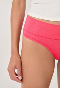 Mutande rosa con una finitura liscia e lucida, taglio a vita bassa, con cuciture a contrasto e una semplice cintura elastica.