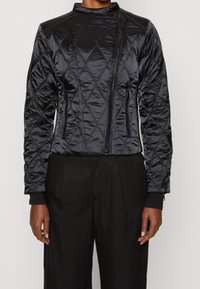 Black quilted bomber jacket with a high collar, zip closure, and two side pockets. Features a smooth texture and elastic cuffs.