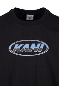 Black cotton t-shirt featuring a large grey and blue oval logo with the text "KANI" in a bold, stylized font. Classic crewneck design.