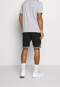 Grå kortärmad skjorta med turkosa detaljer, matchad med svarta shorts med vita ränder. Sneakers och vita strumpor fulländar looken.