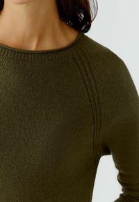 Olivgrüner Strickpullover mit Rundhalsausschnitt, der strukturierte Rippdetails entlang der Schultern und eine glatte Stoffoberfläche aufweist.