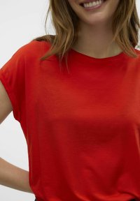 Haut rouge à manches courtes en tissu doux avec une coupe décontractée et un col rond. La texture est lisse avec un léger éclat.