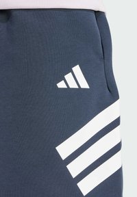 Dark blue sweatpants with white angled stripes and a logo. Made of soft, textured fabric, featuring a side pocket and elastic waistband.