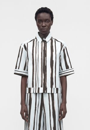 Personne porte une chemise à manches courtes et un pantalon assortis avec des rayures verticales noires et blanches irrégulières sur un fond uni clair.