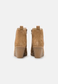 Bottes cheville en daim beige avec talon compensé, fermetures éclair latérales et petites languettes à l'arrière pour un enfilage facile.