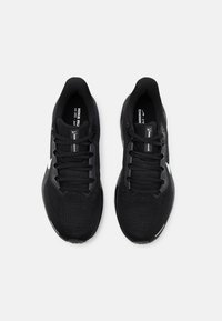 Baskets de sport noires avec une tige en mesh respirant, lacets plats et marquage blanc. Elles disposent d'une semelle rembourrée et d'un design léger.