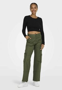 Fekete bordás, hosszú ujjú crop top olíva zöld cargo nadrággal párosítva, amely oldalzsebekkel, laza szabással rendelkezik, és fehér sportcipővel van kiegészítve.