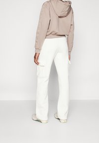 Lys beige cropped hoodie med logodetaljer på ærmerne, parret med hvide cargobukser med sidelommer. Blødt stof med en afslappet pasform.