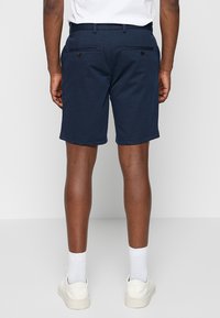 Navy-blaue Baumwollshorts mit schlankem Schnitt, ausgestattet mit zwei Gesäßtaschen mit Knopfverschluss und einer glatten, strukturierten Oberfläche.