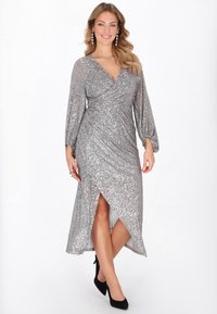 Hopeinen paljettimekko, jossa kietaisuominaisuus, pitkät puffhihat ja korkea halkio. Jokaisessa hihaosassa on rypytetty tekstuuri ranteen läheisyydessä.