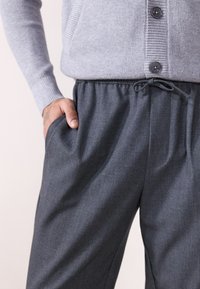 Grijze gebreide cardigan met ribbeltextuur en knopen, gecombineerd met donkerg rijze gepaste joggingbroek met elastieke tailleband en zijzakken.