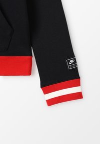 Černý rukáv mikiny s červeným žebrovaným límcem s bílým proužkem. Na spodní straně je nášivka s logem Nike. Měkká textura látky.