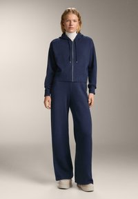 Námornícky dvojdielny outfit pozostávajúci z mikiny na zips a širokých nohavíc, pletená textúra, s šnúrkami na kapucni a rebrovanými manžetami a lemom.