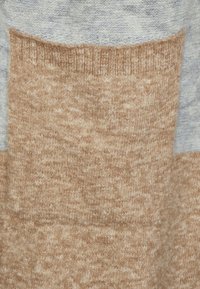 Pletený svetr v kombinaci béžové a světle šedé barvy. Materiál má měkký, texturovaný povrch a jednoduchý design s blokováním barev.