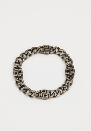Bracelet en métal argenté composé de maillons plats entrelacés et d'accents distincts en forme de carré dans un design patterned.