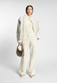 Vit puffjacka med faux pälskrage, ribbad gräddfärgad tröja, gräddfärgade vida byxor och beige spetsiga klackar; håller en taupe handväska.