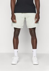 Light green shorts with a loose fit, featuring a rolled hem and logo detail. Paired with white sneakers and crew socks. Black shirt above.