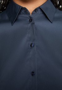 Camicia blu navy con bottoni, realizzata in un tessuto liscio, colletto a punte e bottoni scuri. Presenta un design classico con una leggera lucentezza.