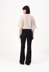 Top en tricot beige à manches larges, associé à un jean noir évasé. Le jean possède des poches arrière et une taille bien ajustée.