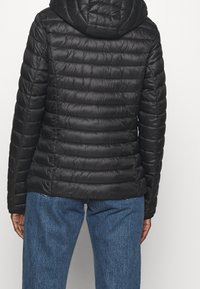 Czarna pikowana kurtka z poziomą teksturą, kapturem i błyszczącym wykończeniem, połączona z jasnoniebieskimi dżinsami z wysokim stanem.