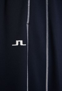 Marinblåt sporttyg med kontrasterande vit sömnad. Har en liten vit logotyp. Texturen är slät, med en åtsittande design.