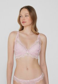 Růžový krajkový bralet s trojúhelníkovým tvarem, květinovým vzorem, průhlednými panely, zvlněnými okraji a centrálním dekoračním knoflíkem.