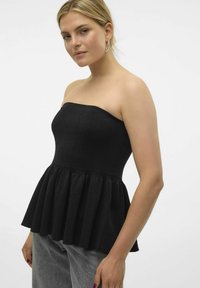 Svart axellös peplumtop i texturerat tyg, med en figurnära bodice och utsvängd plisserad nederkant. Modellen bär grå byxor.