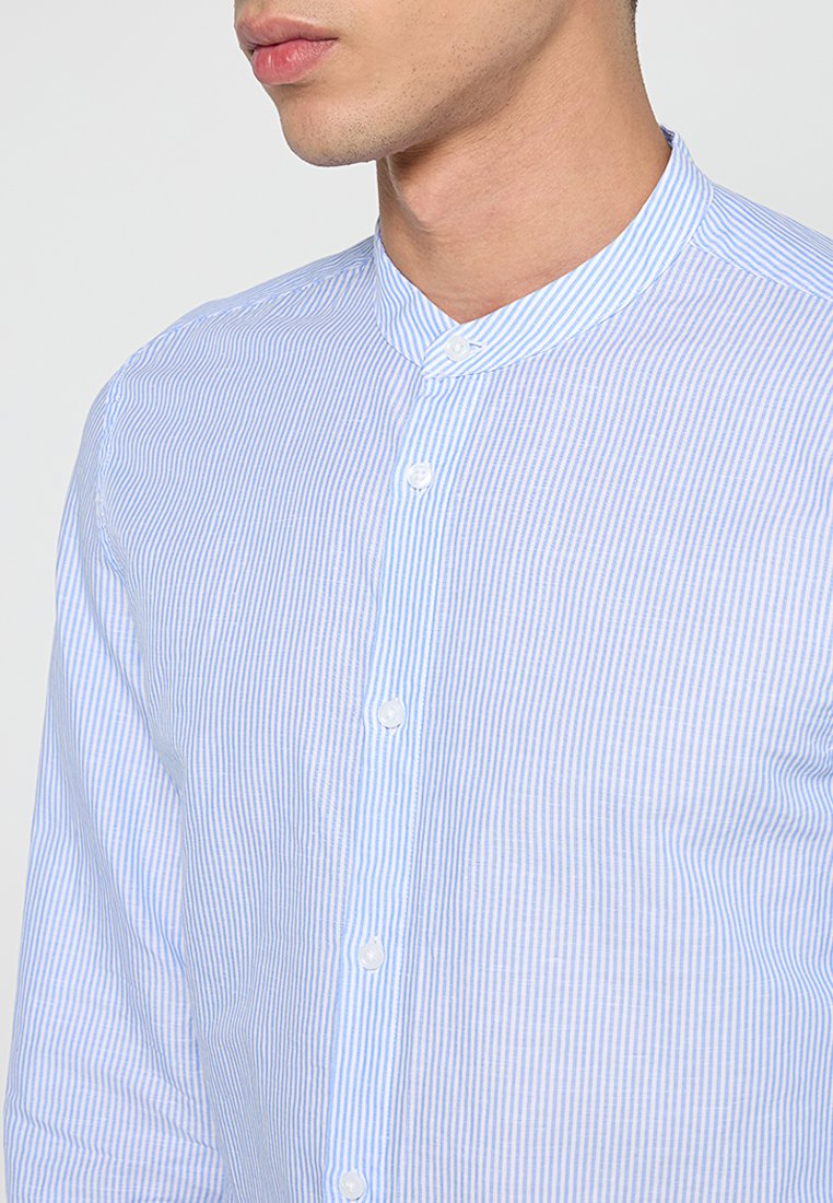 Camicia a righe blu e bianche con colletto alla cinese e una texture liscia. Presenta righe verticali di spessore uniforme e bottoni bianchi.