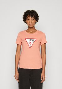 Pink bomulds t-shirt med rund halsudskæring og korte ærmer, med en rød trekantet grafik, hvor der står "GUESS" og et spørgsmålstegn i midten.