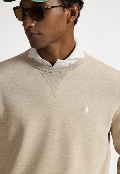 Μπεζ πουλόβερ πλεκτό με V-λαιμόκοψη και γιακά πουκάμισου πόλο σε λευκό χρώμα από κάτω, με μικρό λευκό λογότυπο πόνυ στο στήθος.