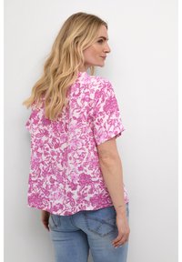 Blusa a maniche corte con motivo floreale rosa e bianco, realizzata in tessuto leggero. Presenta un orlo arrotondato e dettagli con pieghe sul retro.
