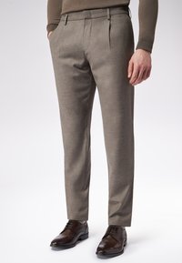 Dopasowane spodnie w jasnoszarym materiale o subtelnej teksturze, z płaskim przodem, kieszeniami bocznymi, zestawione z ciemnobrązowymi butami.