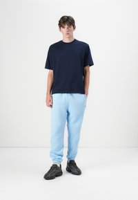 T-shirt en coton marine à manches courtes associé à un pantalon de jogging bleu clair. Baskets noires avec un design texturé et des semelles épaisses.