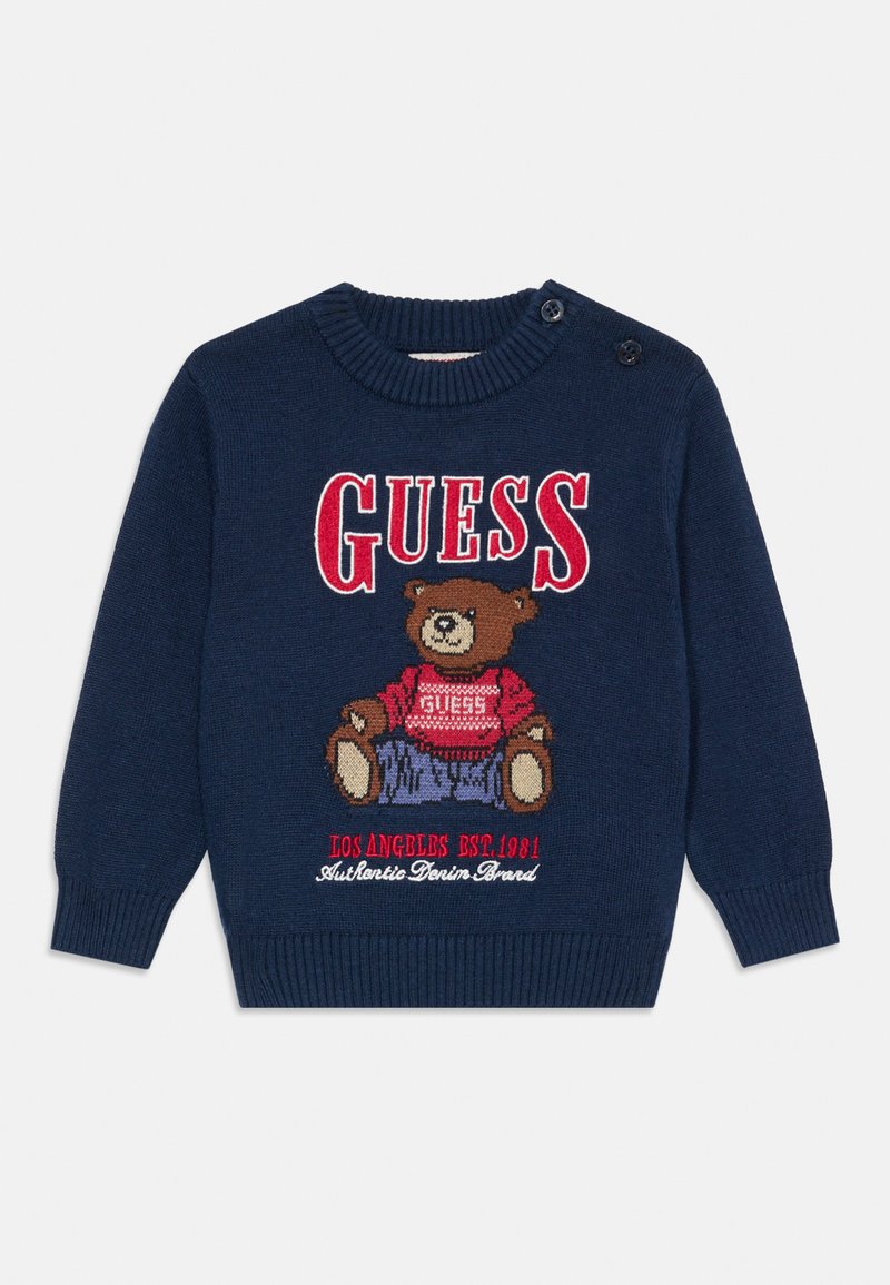 Marineblå barnekjole med rød "GUESS" tekst, en kosebamse iført en rød genser, og broderi av "Los Angeles EST. 1981".