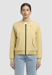 Heled kollane bomber-jakk, millel on lukuga sulgemine, küljetaskud, soonikkoes varrukad ja serv, ning vasakul rinna kohal väike logo.