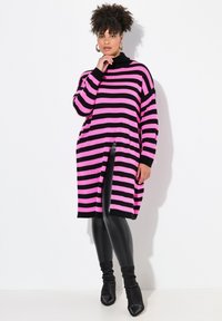 Ylihengittävä neulepaita, jossa on vaaleanpunaisia ja mustia raitoja, ribbaus kaula-aukossa ja sivuaukkoja. Yhdistetty mustiin legginsseihin ja nilkkasaappaisiin.