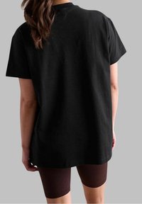 Sort t-shirt med kortærmer og løs pasform, lavet af bomuld. Kombineret med tætsiddende brune ribbede shorts, der går over knæet.