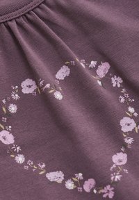 Lila stickad tyg med rynkad halsringning, med en blomstertryck i rosa och vitt, arrangerad i ett cirkulärt mönster i mitten.