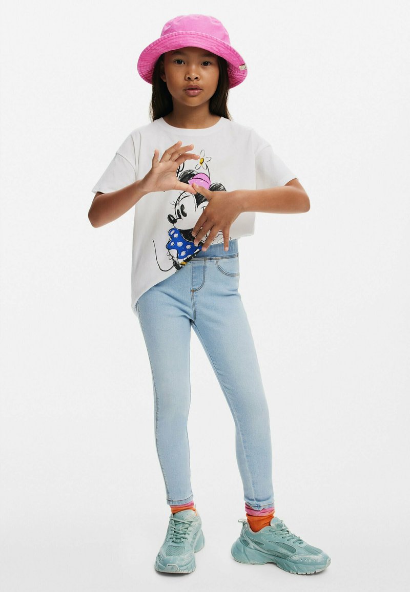 Bílý tričko s grafikou Minnie Mouse, světle modré skinny džíny, růžový kbelíkový klobouk a tyrkysové tenisky se vrstvenými barevnými ponožkami.