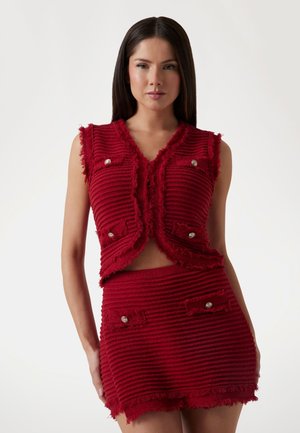 Rode twee-delige outfit met een mouwloze, franjes top met zilveren knopen en een bijpassende skort, beide van textuur ribbed stof.