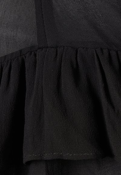 Μαύρο ύφασμα με υφή και ραφή με σούρες που δημιουργεί λεπτομέρεια βολάν.