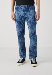 Vaqueros azules con un textura de chapoteo y teñido anudado. Diseño de pierna recta, estilo clásico de cinco bolsillos, combinados con zapatillas en blanco y negro.