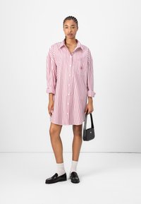 Randig skjortklänning i röd och vit med en knapp-up design, långärmad, bröstficka, och matchad med en svart handväska och loafers.