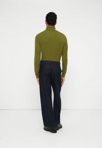 Zelena rebrasta turtleneck punca, prilagodljiva u gornjem dijelu, u kombinaciji s opuštenim tamnoplavim trapericama, koje imaju jednostavan dizajn i stražnje džepove.