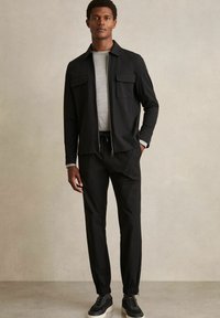 Black zip-up jacket with two front pockets, paired with matching trousers featuring elastic cuffs. Grey crew-neck shirt underneath.