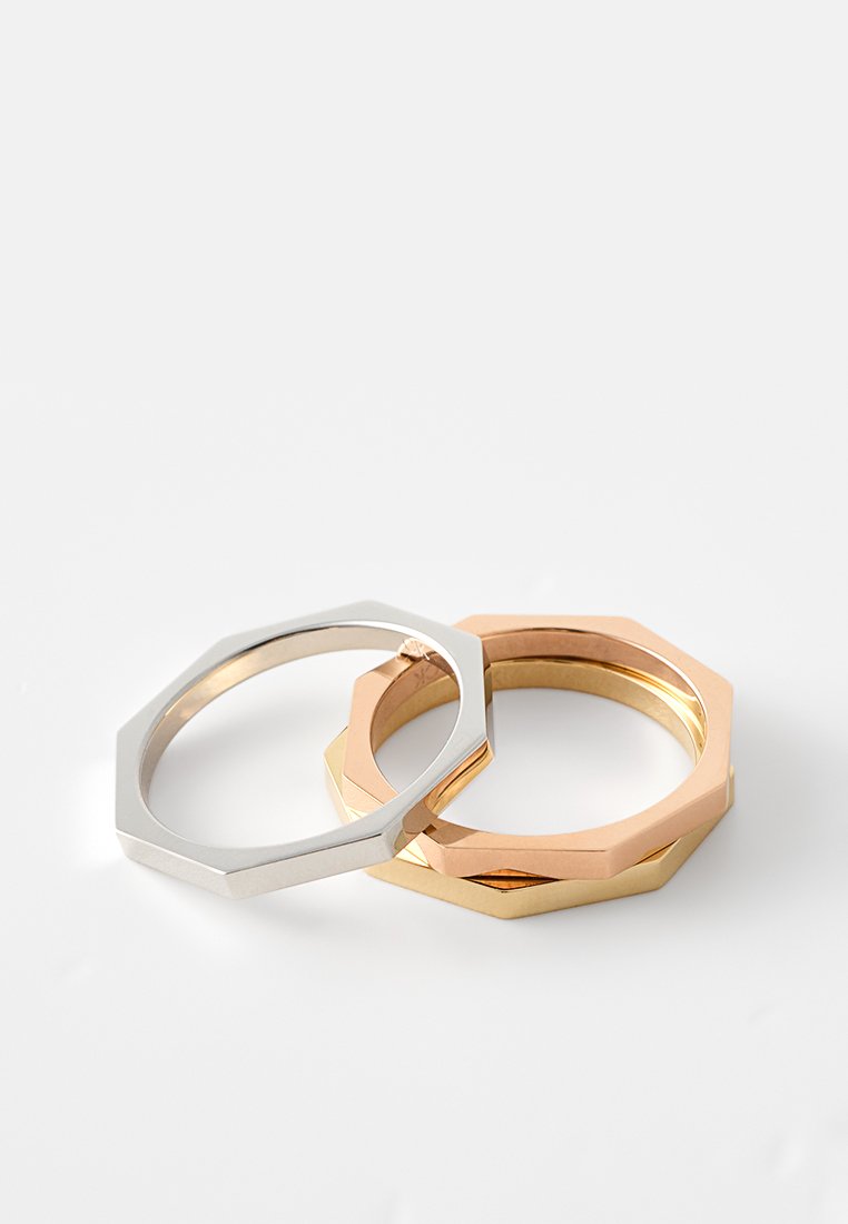 Dos anillos octagonales, uno plateado y otro de oro rosa, con un acabado metálico suave y bordes geométricos limpios.