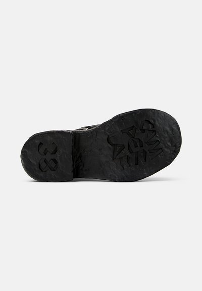 Black sneaker sole with textured grip pattern and subtle embossed details. Thick rubber material, slightly worn appearance, no visible branding.