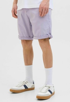 Jasnofioletowe szorty z zawiniętymi mankietami, wykonane z gładkiego materiału. Połączone z białymi trampkami z granatowymi akcentami i ribbowanymi białymi skarpetkami.